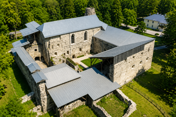 Aerial view of a historic stone building with a metallic roof surrounded by trees.