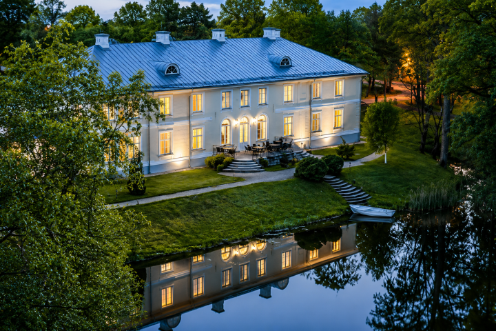Elegant mansion with lit windows, reflecting in a calm pond at dusk.
