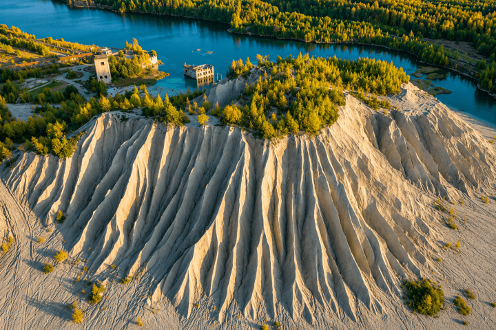 Aerial view of sand dunes with green trees and blue lakes.