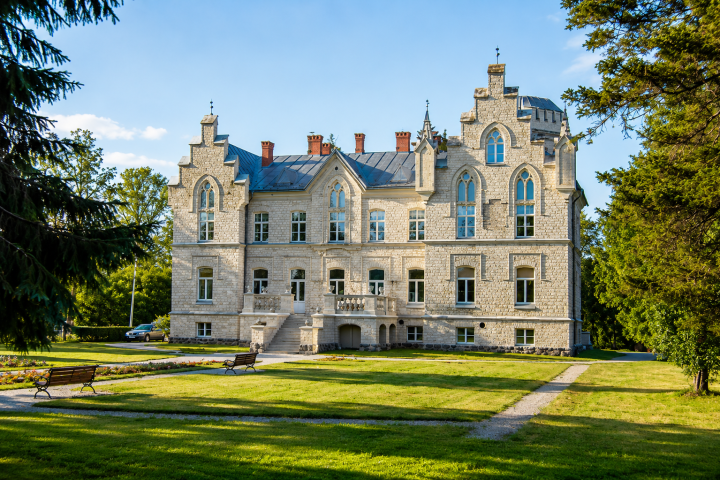 Historic stone mansion with arched windows, surrounded by trees.