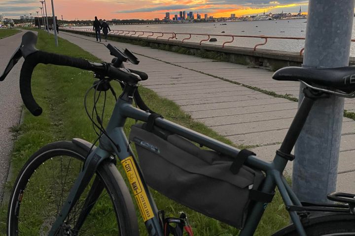 Bicycle by a waterfront path at sunset with city skyline in distance.